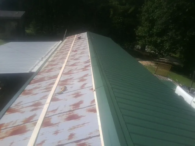 Old rusted panels beside newly installed green metal roofing — Wind Damage Roof Repair by Roofing Brothers in Chuckey