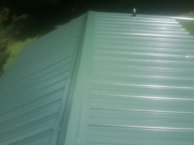 New green metal panels meeting at the ridge of a roof — Flat Roof Repair work by our crew in Chuckey