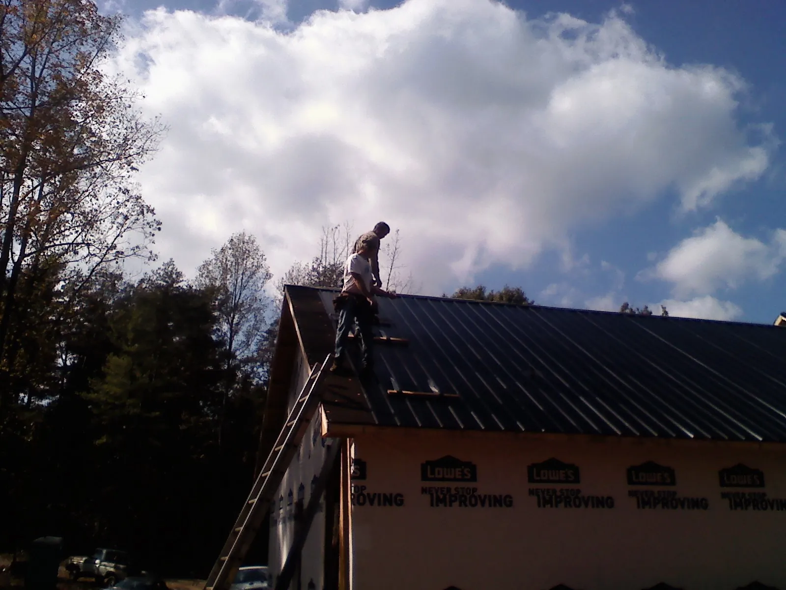 Roofer fastening dark metal panels high against a cloudy sky, from a Roof Inspection job in Chuckey