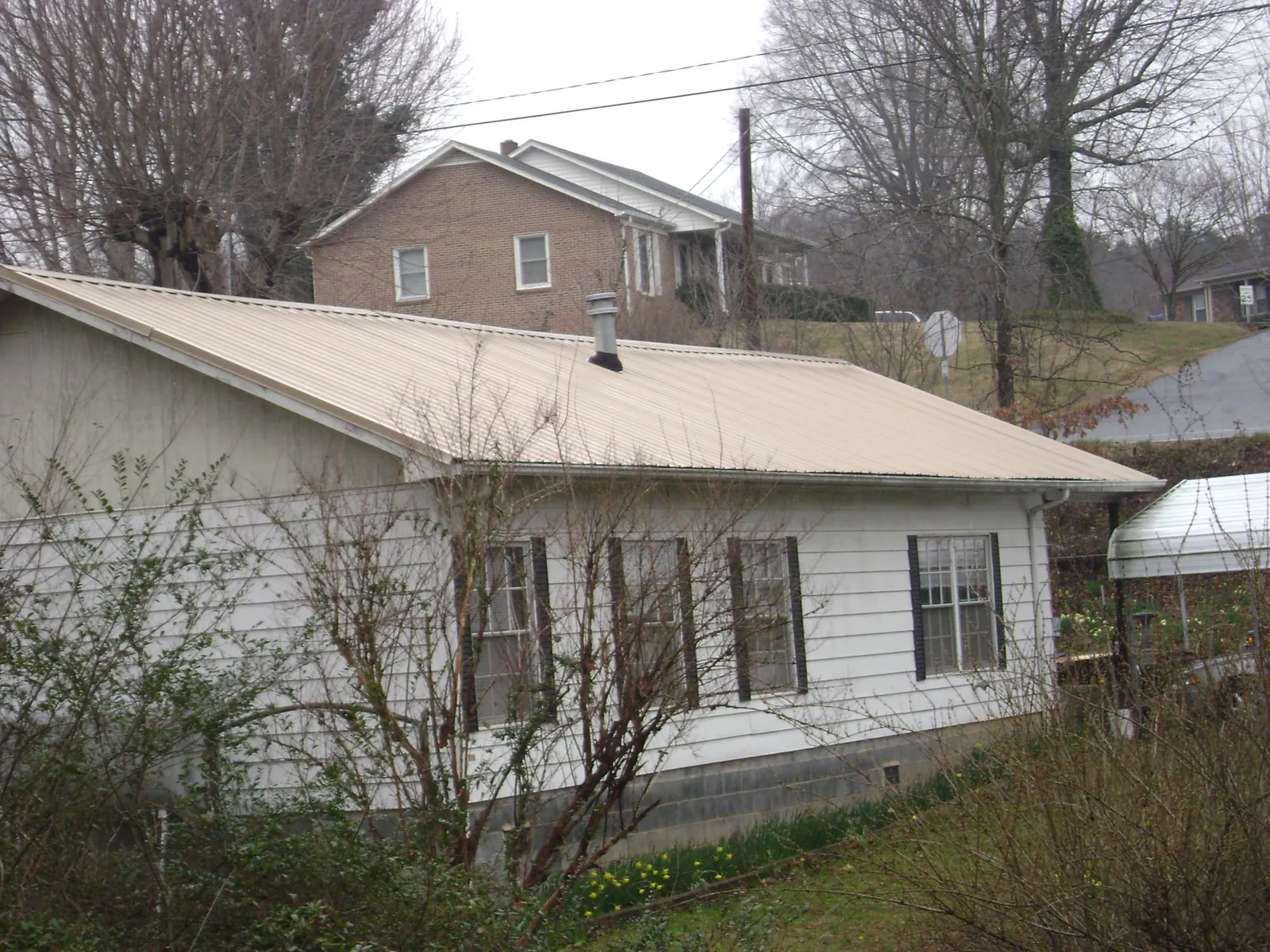 Tan metal roof on a white sided house set into a hillside — Commercial Roofing by Roofing Brothers in Chuckey