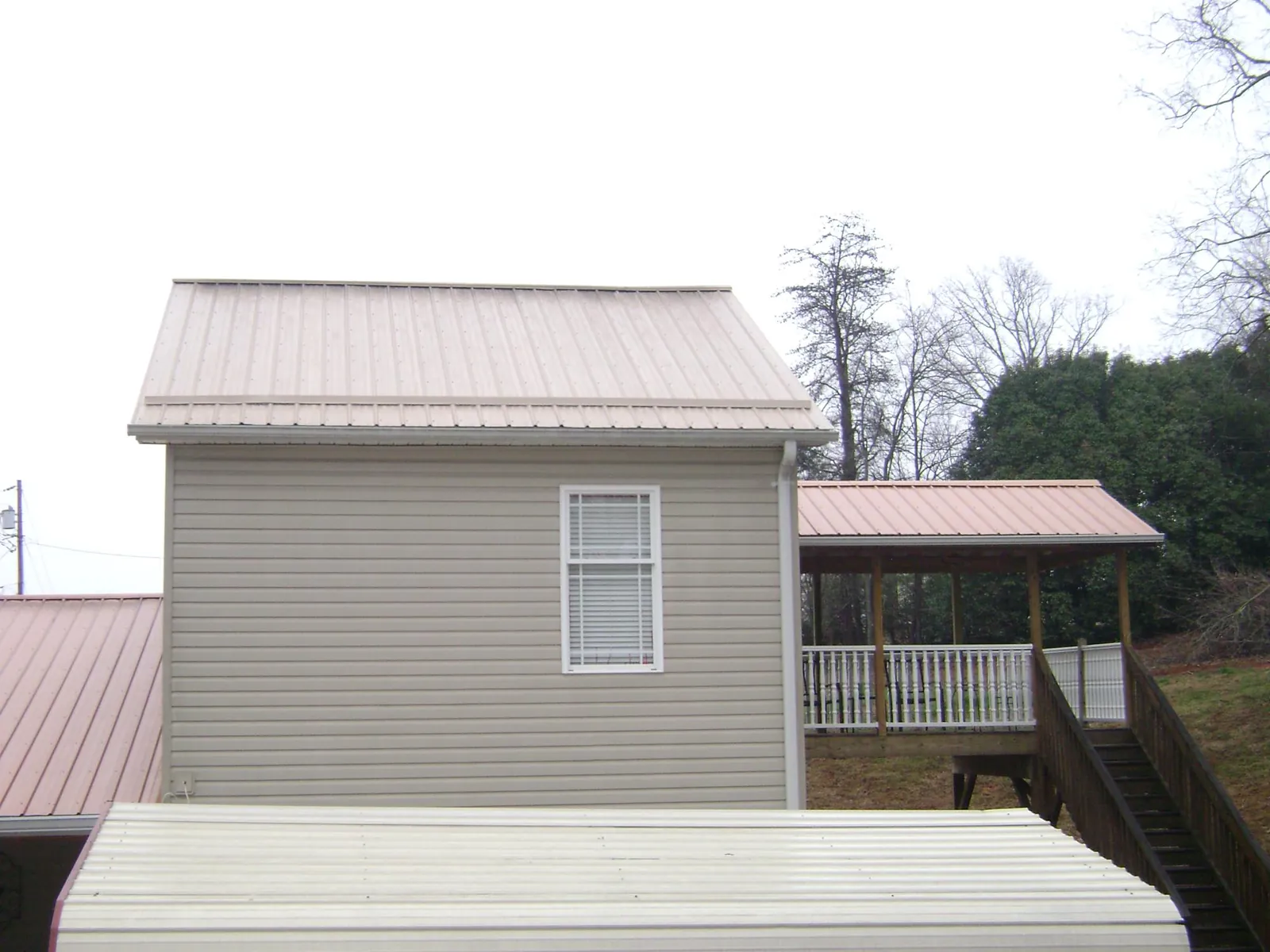 Tan metal roofs on a two story addition and attached porch, from a Roof Replacement job in Chuckey